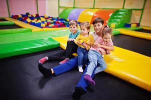 niños jugando en el centro de juegos interior y sentados en un trampolín. familia numerosa con cuatro hijos. foto