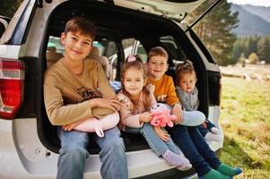 Family of four kids at vehicle interior. Children sitting in trunk. Traveling by car in the mountains, atmosphere concept. photo