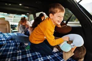 Two brothers fighting pillows at vehicle interior. Children in trunk. Traveling by car in the mountains, atmosphere concept. photo