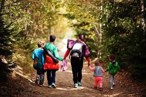 Back of mother with four kids walking on wood mountains. Family travel and hiking with childrens. Wear backpack. photo