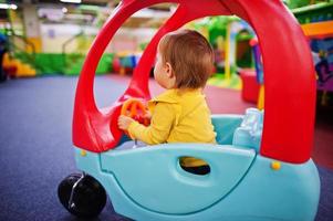 Cute baby girl rides on a plastic car in indoor play center. photo