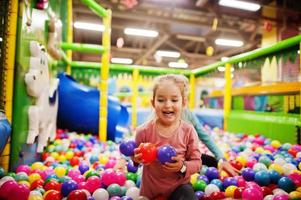 Child playing in colorful ball pit. Day care indoor playground. Balls pool for children. Kindergarten or preschool play room. photo