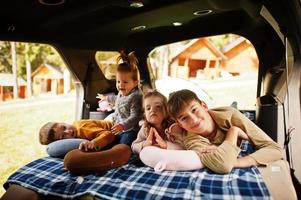 Family of four kids at vehicle interior. Children in trunk. Traveling by car, lying and having fun, atmosphere concept. photo