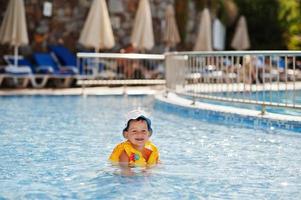 Boy in panama and child life vest bathes in the pool. photo