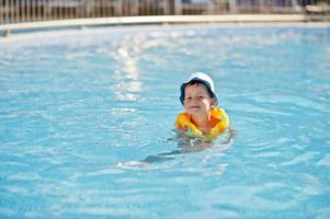 Boy in panama and child life vest bathes in the pool. photo