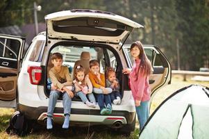 Family of four kids and mother at vehicle interior. Children sitting in trunk. Traveling by car in the mountains, atmosphere concept. photo