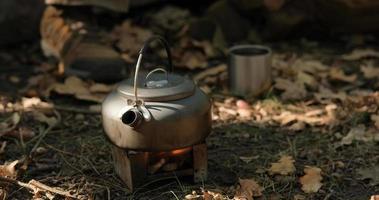 close-up de fogão de combustível sólido com chaleira de água em chamas, chá ou café preparando ao ar livre