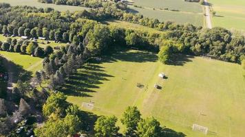 voetbalveld op het platteland, onder bosgebied op zonnige dag. luchtfoto van drone van lokaal voetbalveld op landelijke locatie, met dicht bos rond het gebied. concept van bestemming video