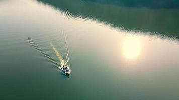 Small speed boat sailing on dark river, leaving trails on water behind at twilight. Above view of water craft sailing along rocky shores on calm lake on sunset in autumn.Concept of water activities video