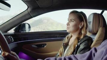 A Bentley passenger girl says something to the driver, the strokes his right arm.Background trees,mountain video