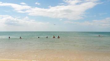 persone sulla spiaggia di mai khao nuotano nel mare e guardano l'aereo di linea che si avvicina all'aeroporto di phuket. video