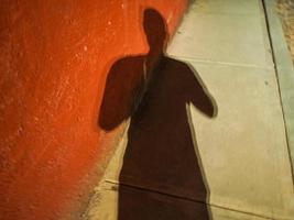Shadow of a man against a red wall and cement sidewalk at night photo