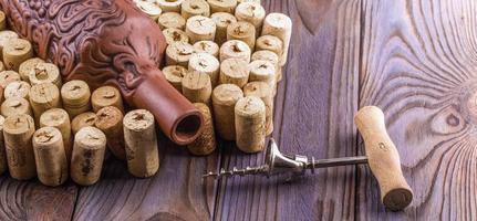 Clay bottle, metal corkscrew and cork on a wooden table. photo