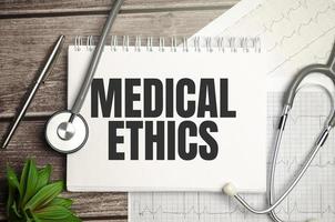 Medical ETHICS text in a notebook with stethoscope on wooden background photo