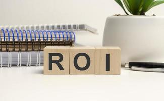 Concept word ROI on wooden cube with notebooks photo