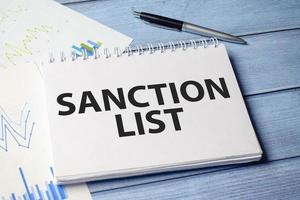 Text Sanction list on white note paper affixed to a notepad on the table photo