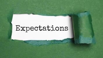 expectations. text on white paper over torn paper background. photo