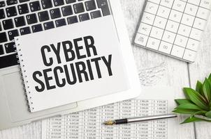 cyber security word on the notebook and pen, laptop on the wooden background photo