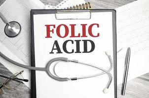 The desktop has a stethoscope, a blue pen, and a gray file folder with the text FOLIC ACID photo