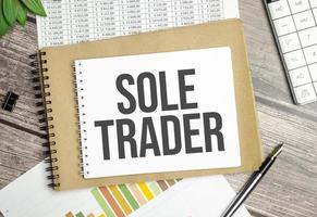 SOLE TRADER text on notebook on the chart with plant, pen and calculator photo