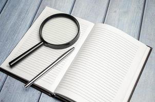 Magnifier glass and empty notebook on wooden background photo