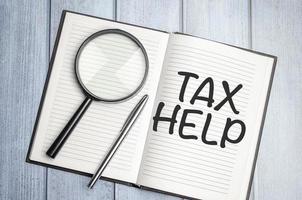 tax help word on notepad with magnifier on wooden background photo