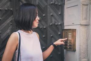 chica que está presionando un botón del intercomunicador de la casa al aire libre frente a una enorme puerta antigua. foto
