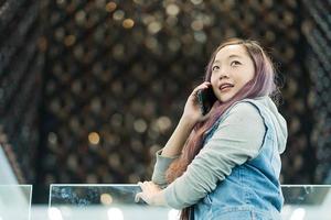 Cheerful young woman in casual wear having telephone conversation standing in mall, smiling female freelancer calling to colleague for share good news about business photo