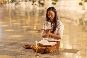 Asia woman wearing traditional dress of Thailand reading Sanskrit ancient Tripitaka book and Dharma book of Lord Buddha dhamma in night. candle lantern photo