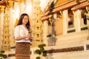 portrait young asian woman wearing traditional dress of Thailand holding candle and walking around at Wat Suthat Thepwararam Bangkok photo