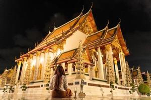 Asian buddhist woman wearing traditional dress of Thailand sitting for meditation to pay respect to Buddha statue at Wat Suthat Thepwararam on Buddhist holy day, Buddhist sabbath day, photo