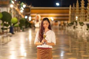 portrait young woman is smileing  holding candle and praying at Wat Suthat Thepwararam in night photo