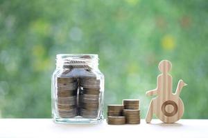 hombre en silla de ruedas y moneda de oro en la botella de vidrio sobre fondo verde natural, ahorre dinero para prepararse en el futuro y el concepto de persona discapacitada foto