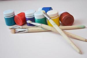 Artistic jars with multi colored gouache paints and brushes, close up. Working materials for drawing, creativity, hobby. photo