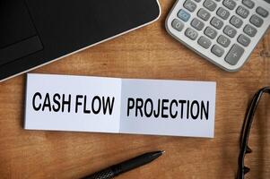 Cash flow projection text on notepad with calculator, pen and laptop background. Business concept photo