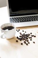 una taza de café, computadora portátil y granos de café esparcidos foto