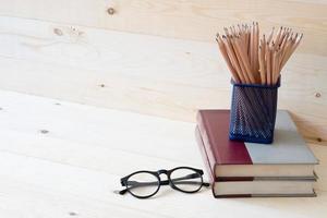 Book with  pencils in basket and eyeglassesl on wooden table background photo