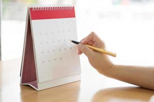 Woman hand carrying calendar and pointing on it by pen photo