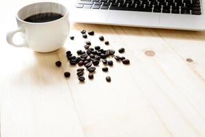 una taza de café, computadora portátil y granos de café esparcidos foto