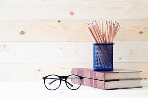 Book with  pencils in basket and eyeglassesl on wooden table background photo