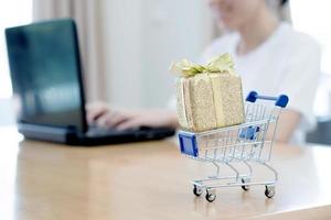 mano que sostiene la computadora portátil con un pequeño carrito de compras foto