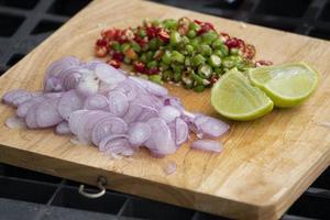 guarniciones de cebolla roja, chile fresco, lima se cortan en rodajas en una tabla de cortar de madera. juego de comida para cocina tailandesa. foto