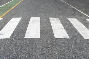 White road crosswalk or crossing path on asphalt road. The pedestrian control path is painted green beside of the road. photo