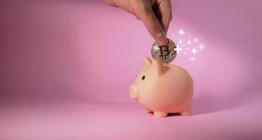 Hand of man drops metal bitcoin coin into piggy bank. Business and Finance. photo