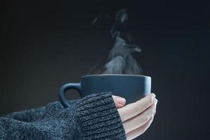 Hands of young girl with a hot Cup of tea on a dark background. Steam rises from the hot drink. photo
