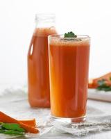 jugo de zanahoria en botella y un vaso y rodajas de fruta fresca aislado sobre fondo blanco. foto