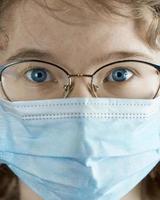 Portrait of a young girl in glasses and a medical mask close-up. Flu epidemic, dust allergy, protection against virus. Coronavirus pandemic. photo