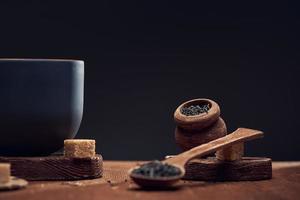 té seco en cucharas de madera y en un tarro de madera y trozos de azúcar de caña sobre la mesa, sobre fondo oscuro. foto