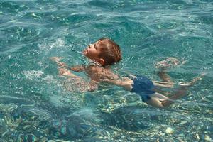 Child boy learning to swim in clear transparent sea. photo