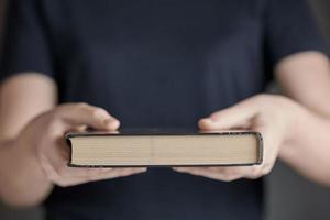 manos de una niña sosteniendo un libro cerrado sobre un fondo gris. foto